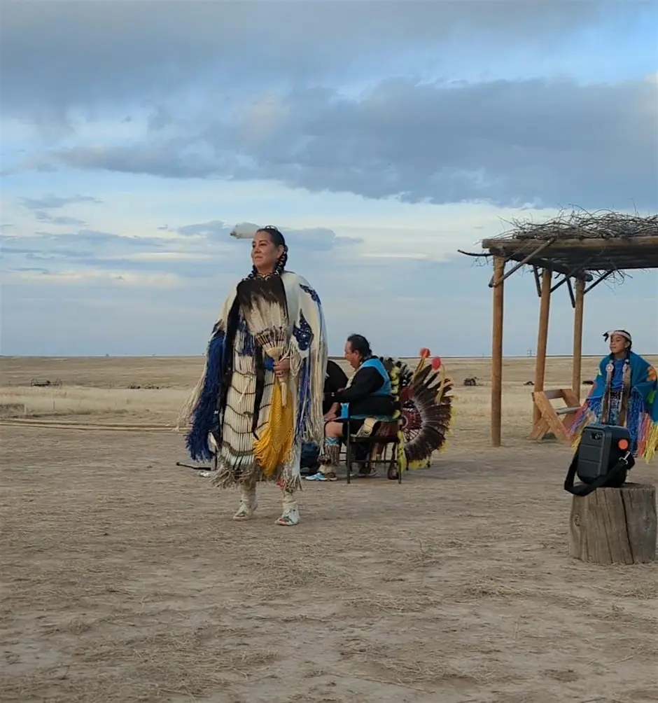 Native dancers in regalia performing outdoors on an open prairie landscape during a cultural storytelling program.