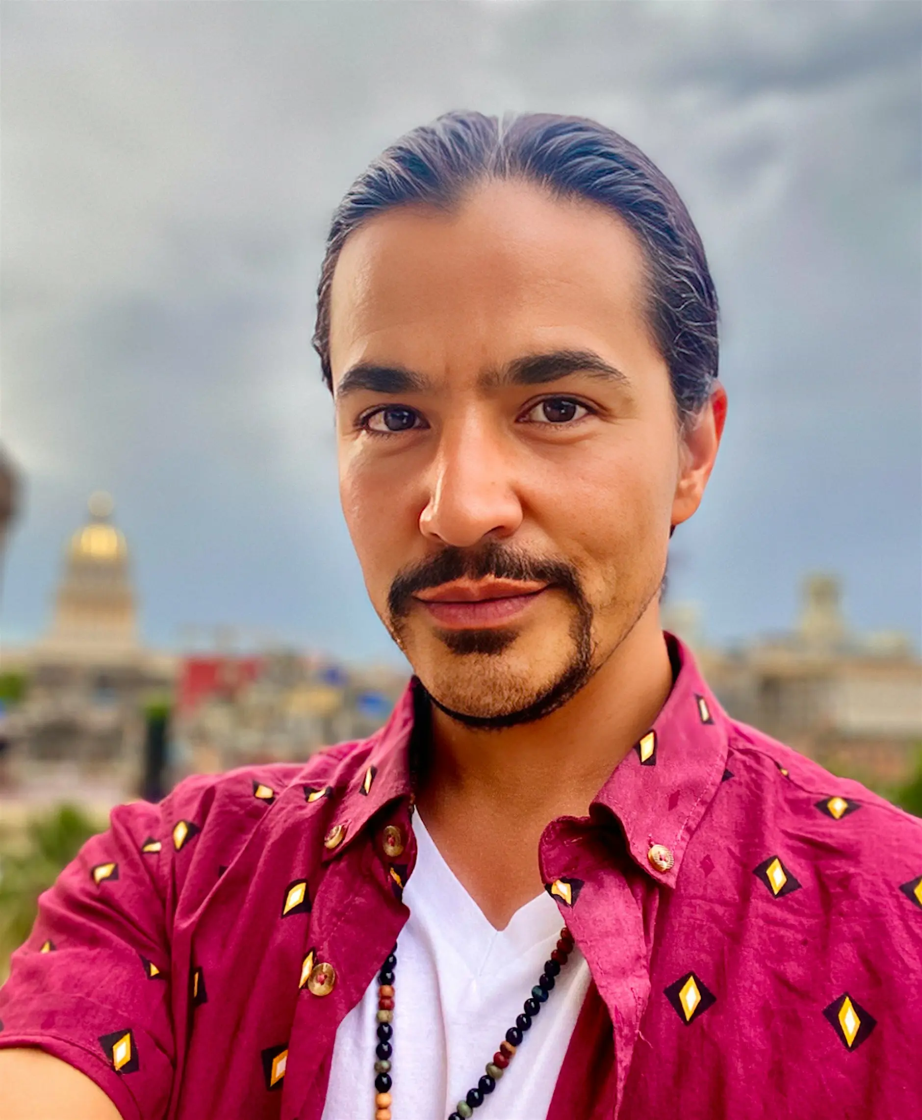 Portrait of an Indigenous artist wearing a magenta patterned shirt with a blurred city skyline in the background.