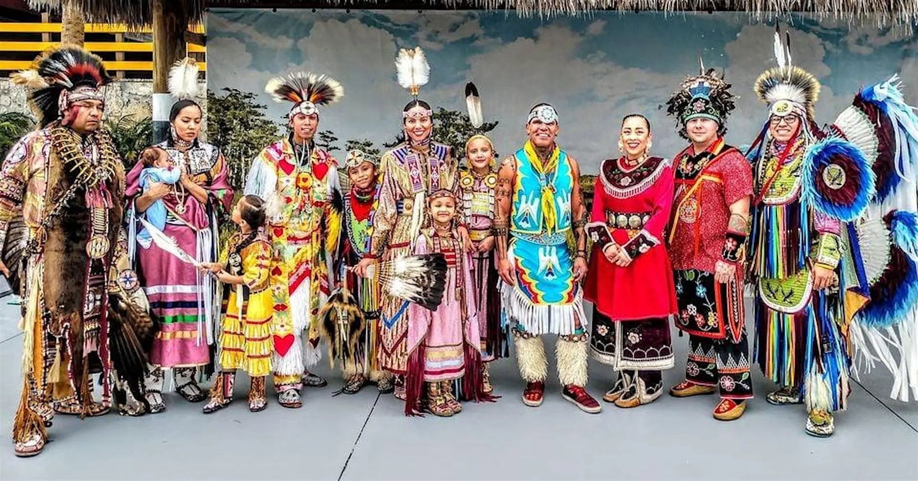 Native American dancers and community members in colorful regalia gathered together at a pow wow celebration.